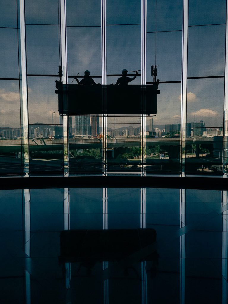 Two people sitting on a bench in front of a large glass window in a government building.